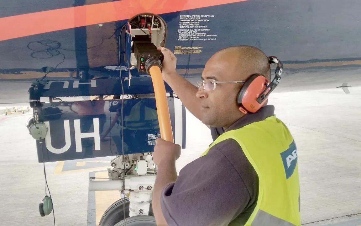Técnico con protección auditiva conectando un equipo de apoyo en tierra al fuselaje de una aeronave